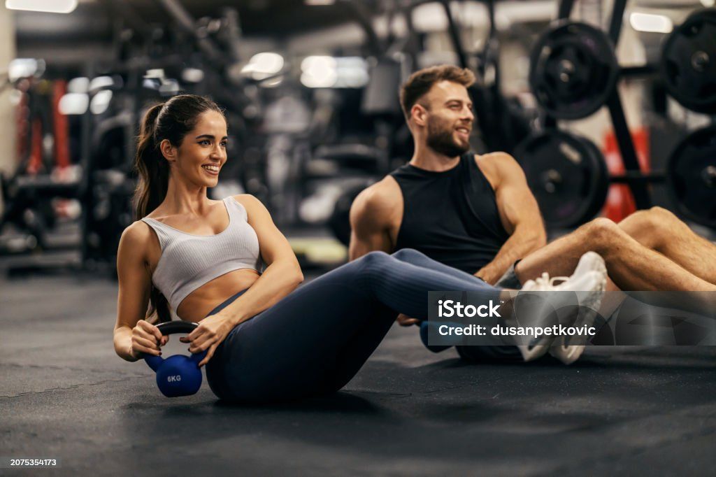 Woman leaning back and rotating a small blue kettlebell during a seated core exercise