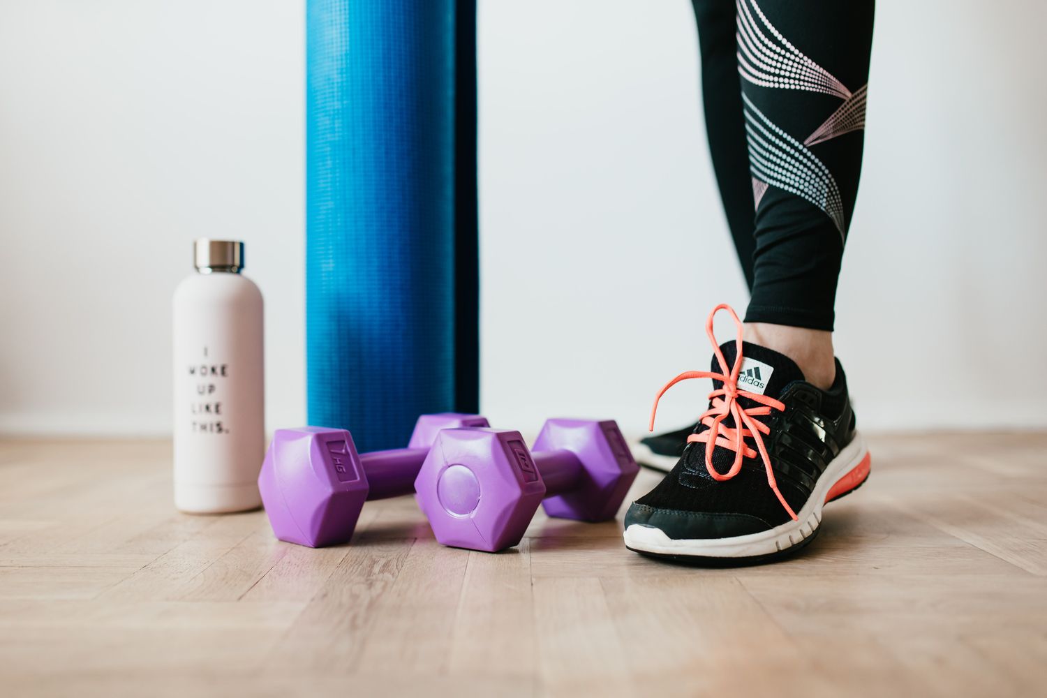 Pair of purple dumbbells, blue exercise mat and white water bottle on a wooden floor
